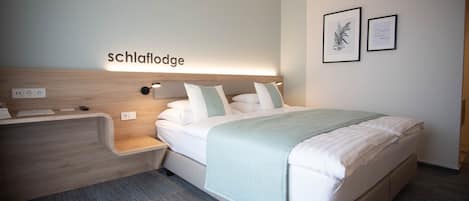 Een moderne hotelkamer met een bed, nachtkastje en een hoofdeinde met verlichting.