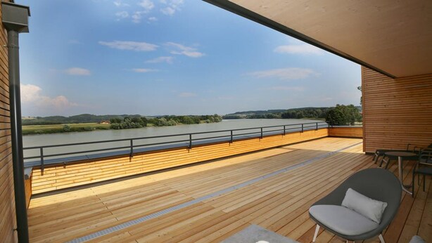 A wooden deck with a view of a river and hills, a chair, and a table.