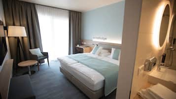 A hotel room with a bed, a desk, a chair, a lamp, and a bathroom with a mirror and shower.