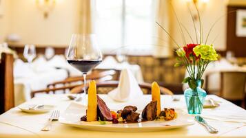 A dining table with a plate of food, a wine glass, and a vase with flowers.