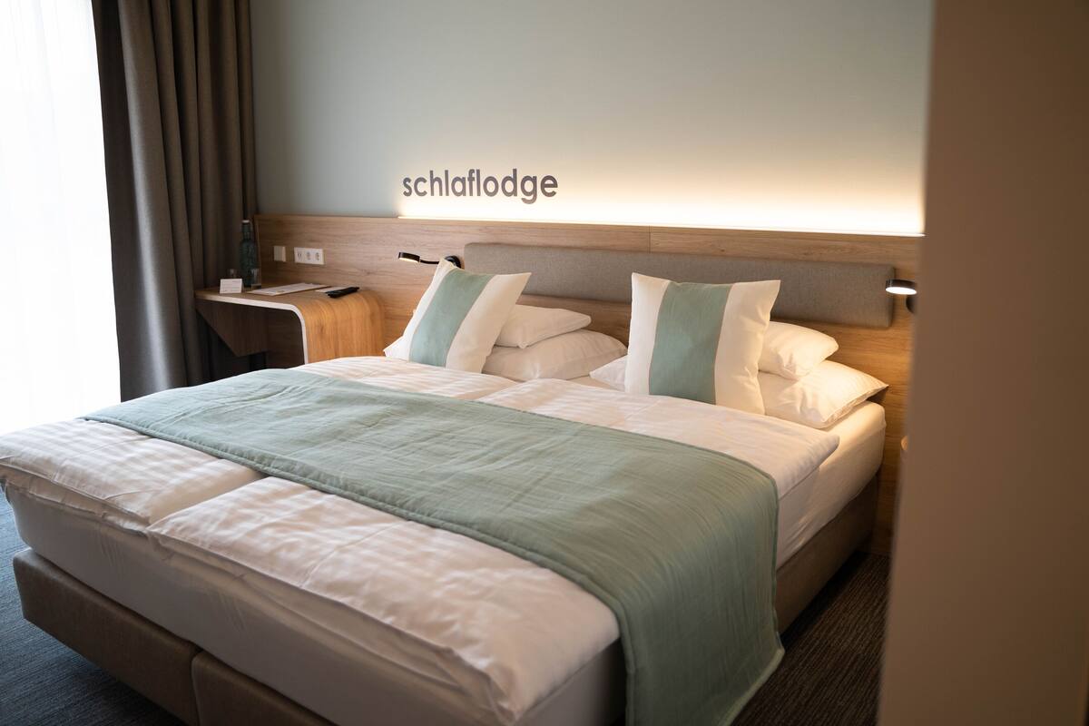 A hotel room with a bed, nightstands, a lamp, and a sign reading "schlaflodge".