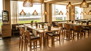 A dining area with wooden tables and chairs, hanging pendant lights, and large windows with a view of a body of water.