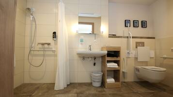 A bathroom with a shower, sink, toilet, and a small shelf with towels.