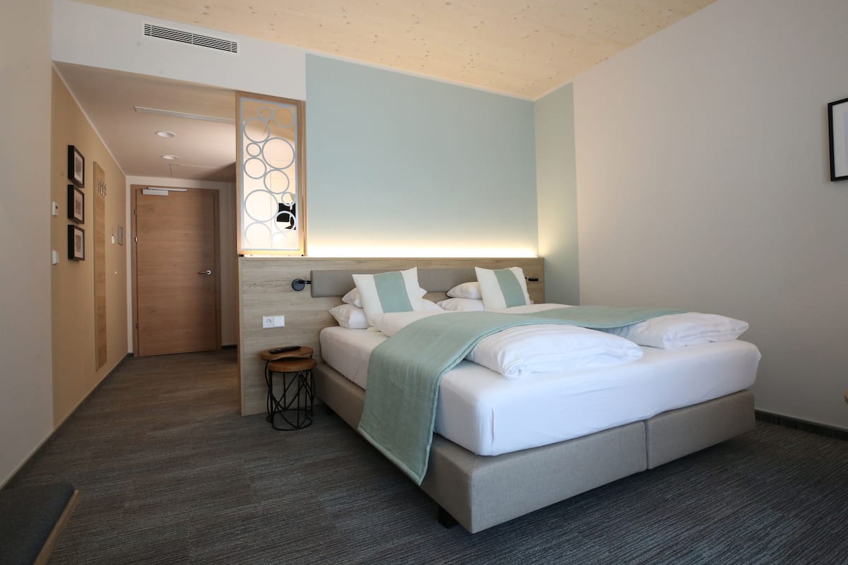 A modern hotel room with a large bed, a bedside table, and a decorative wall panel.