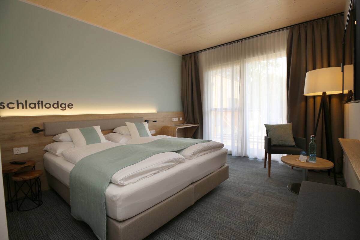 A hotel room with a bed, a desk, a chair, a lamp, and a window with curtains.