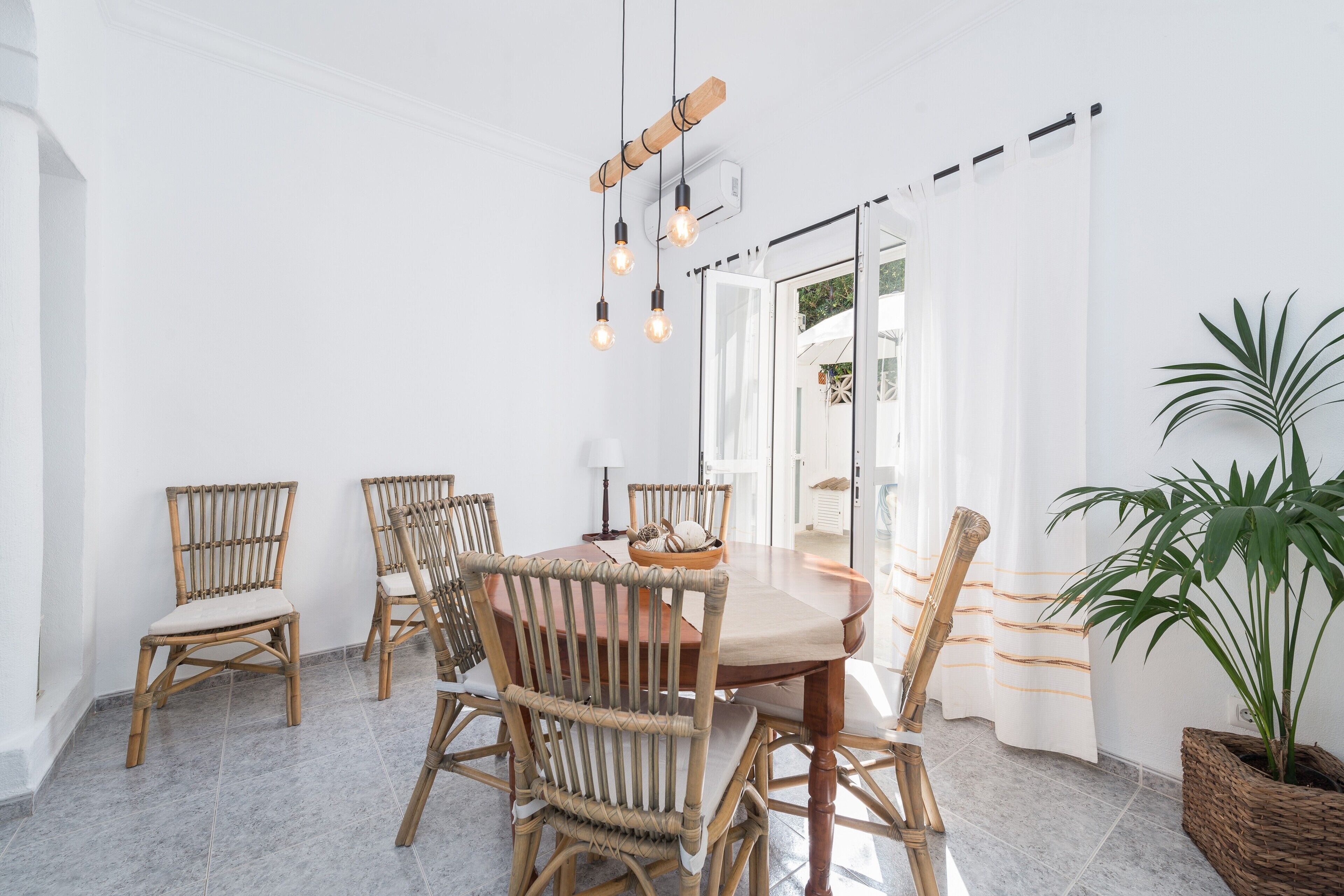 Un comedor con una mesa redonda, seis sillas de mimbre y lámparas colgantes.