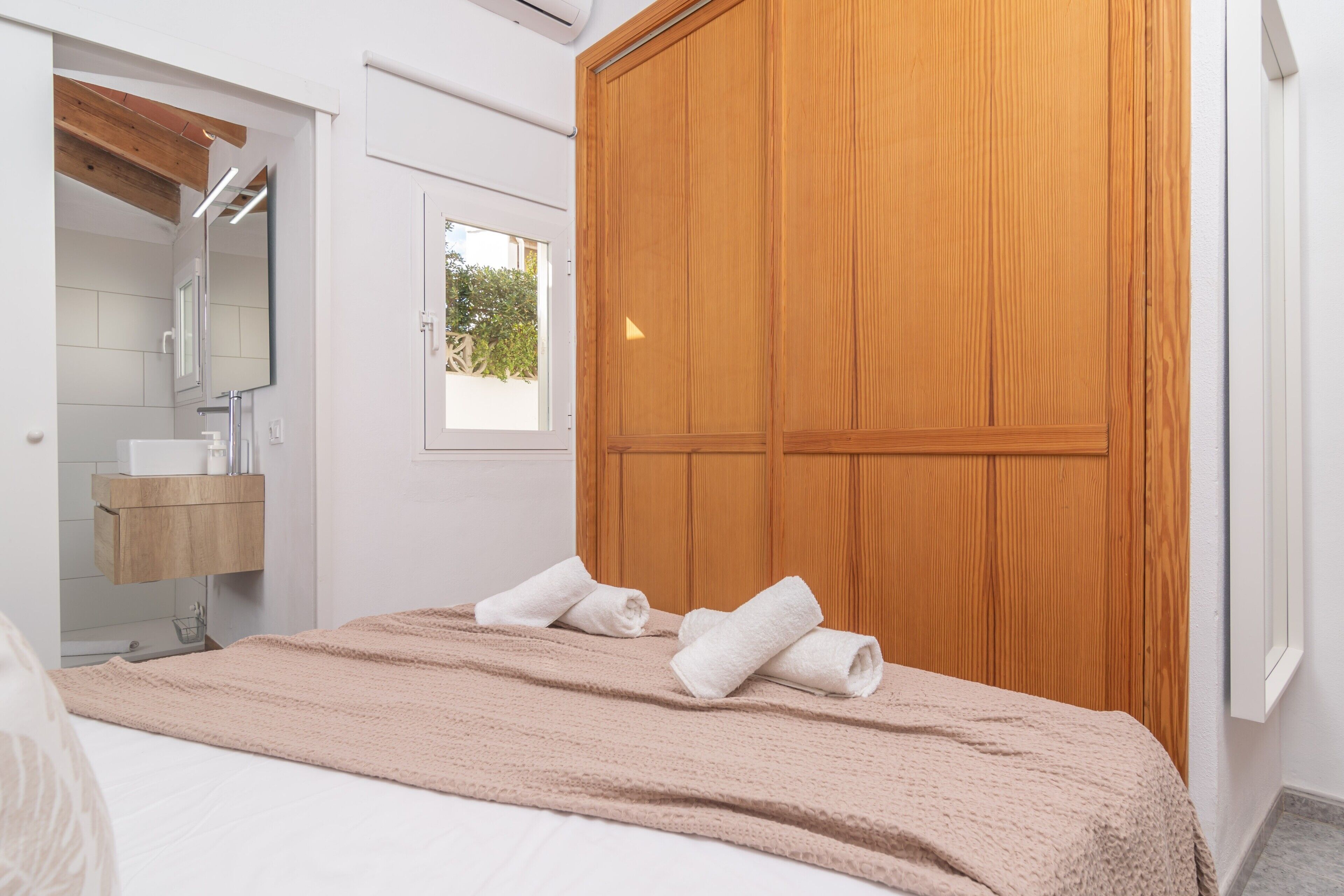 Quarto com armário de madeira, cama com manta bege e banheiro com toucador de madeira.