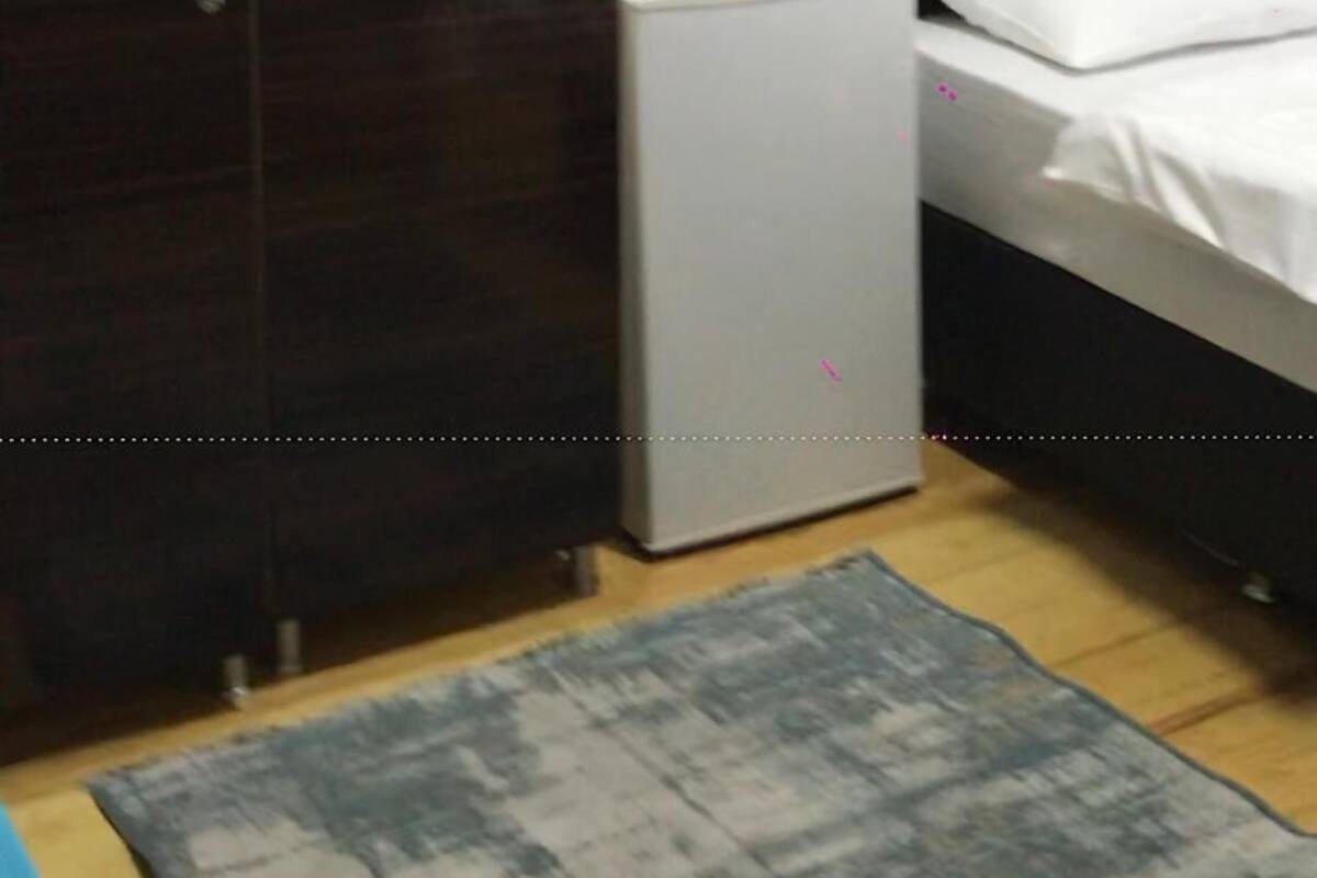 A bedroom with a wardrobe, a small fridge, a bed, and a rug.