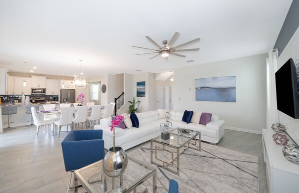 A modern living room with a white sofa, blue chairs, a glass coffee table, and a ceiling fan. - (JD8821) Champions Gate 6/6, Private Pool with Spa & Free Waterpark (Kissimmee)