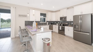 A modern kitchen with white cabinets, stainless steel appliances, and a bar area with bar stools. - (JD8821) Champions Gate 6/6, Private Pool with Spa & Free Waterpark (Kissimmee)