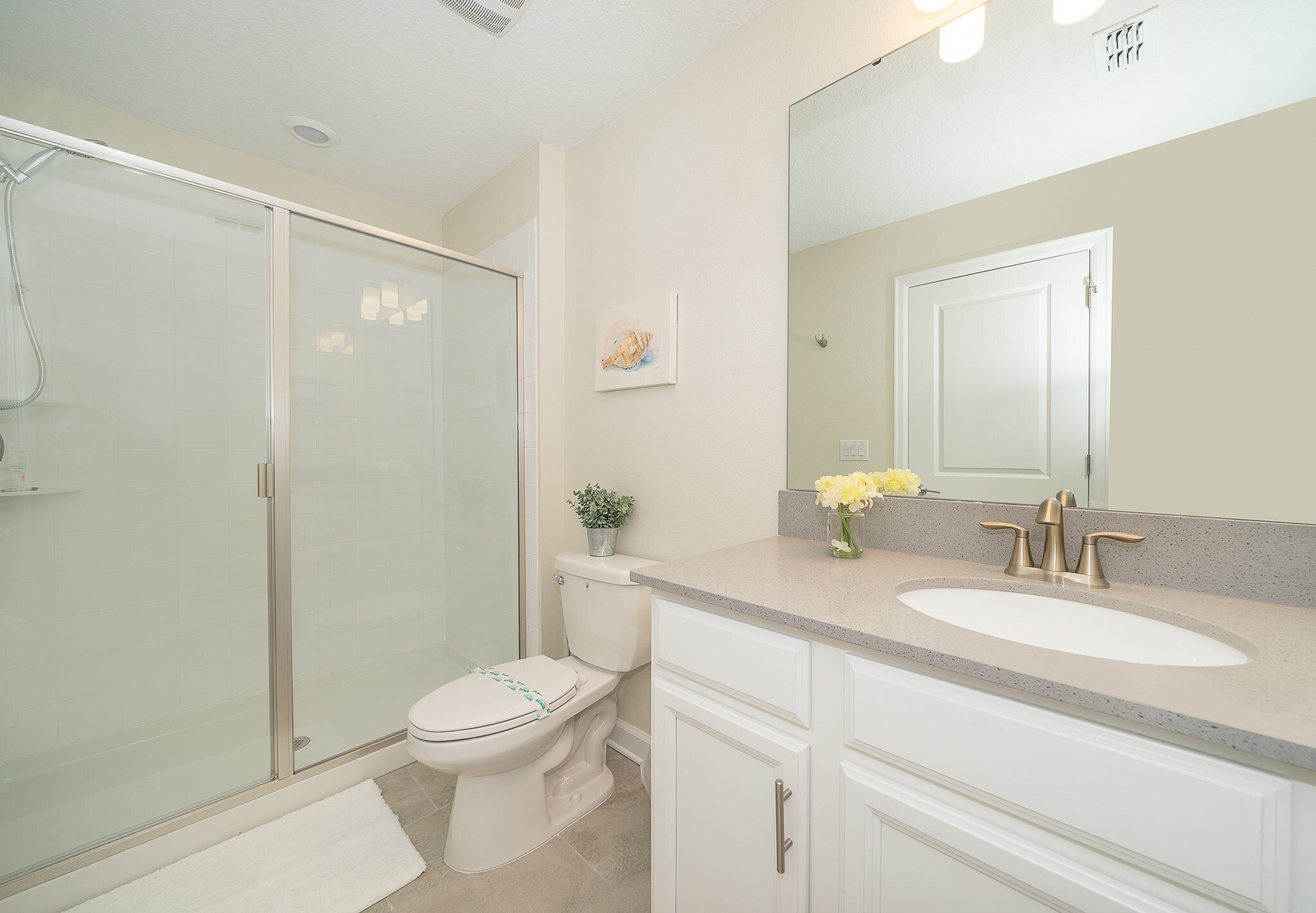 A bathroom with a glass shower enclosure, a toilet, a sink with a mirror, and a small potted plant.
