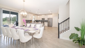 A modern kitchen with white cabinetry, a stainless steel refrigerator, and a dining area with white chairs and a table set for six. - (JD8821) Champions Gate 6/6, Private Pool with Spa & Free Waterpark (Kissimmee)
