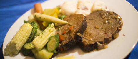 Une assiette remplie de nourriture, comprenant de la viande, des légumes et un aliment de couleur claire, peut-être du poisson, le tout posé sur une nappe bleue.