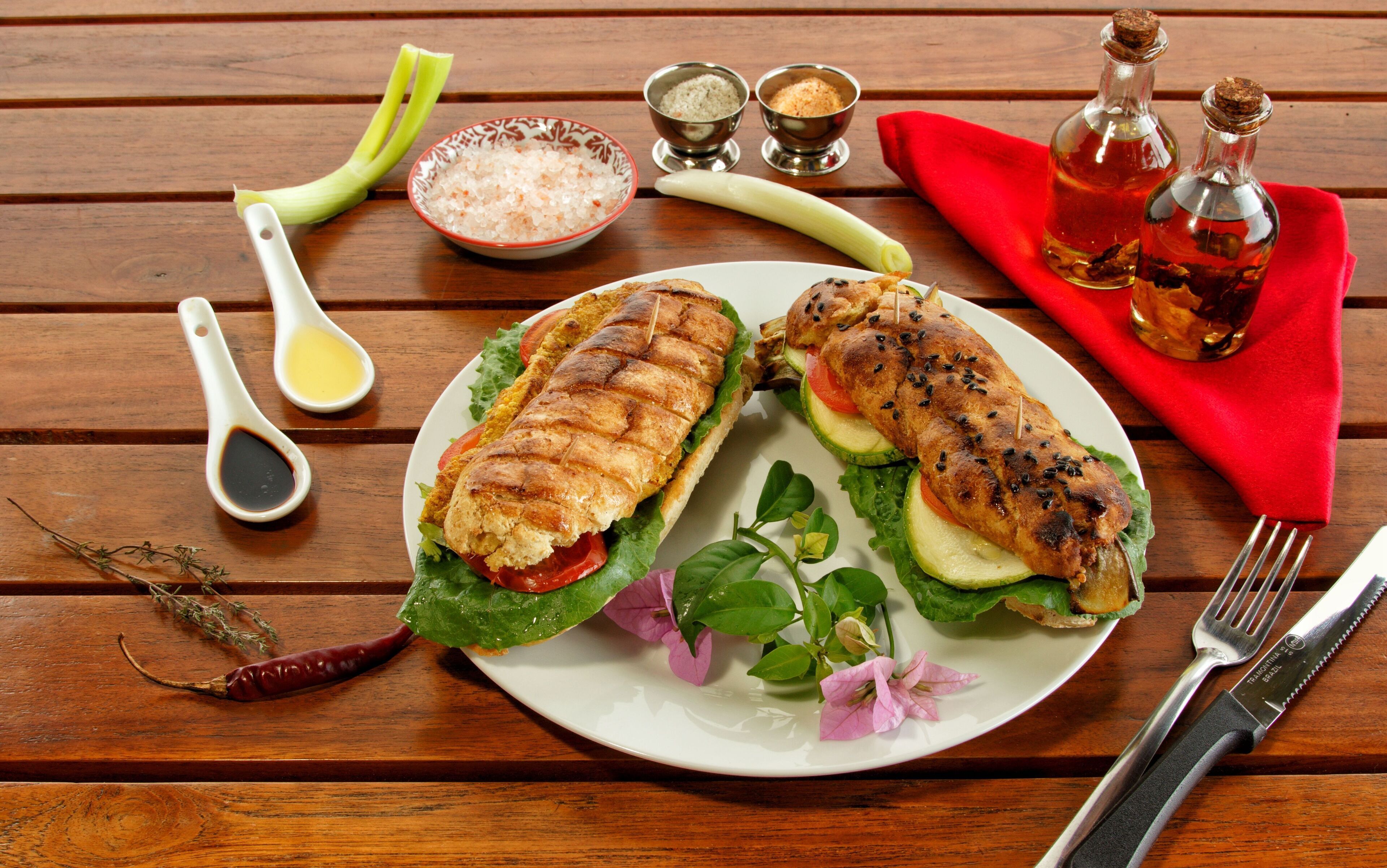 A plate with grilled chicken sandwiches, a red napkin, and condiments on a wooden table.