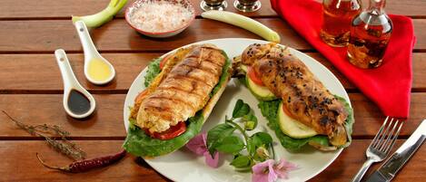 A plate with grilled chicken sandwiches, a red napkin, and condiments on a wooden table.