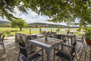 An outdoor deck with wooden furniture, a view of a golf course, and a lake in the background. - Blue Bay Beach Apartments (Sint Michiel)