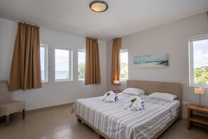 A bedroom with a large bed, two bedside tables, a chair, and a painting on the wall. - Blue Bay Beach Apartments (Sint Michiel)