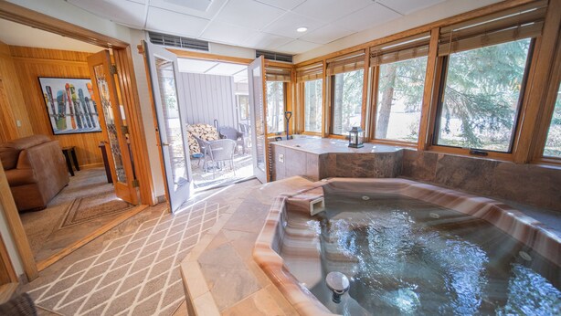 Een wellnessruimte met een jacuzzi, houten wanden en grote ramen.