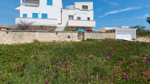 Un bâtiment moderne aux murs blancs, agrémenté de volets bleus, d’un mur en pierre et d’un espace verdoyant parsemé de fleurs.