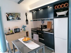 Eine moderne Küche mit Mikrowelle, Toaster und Kaffeemaschine auf der Arbeitsplatte. Auf dem Tisch steht eine Obstschale und eine Weinflasche. Die Küche hat dunkle Schränke und einen weißen Kühlschrank.