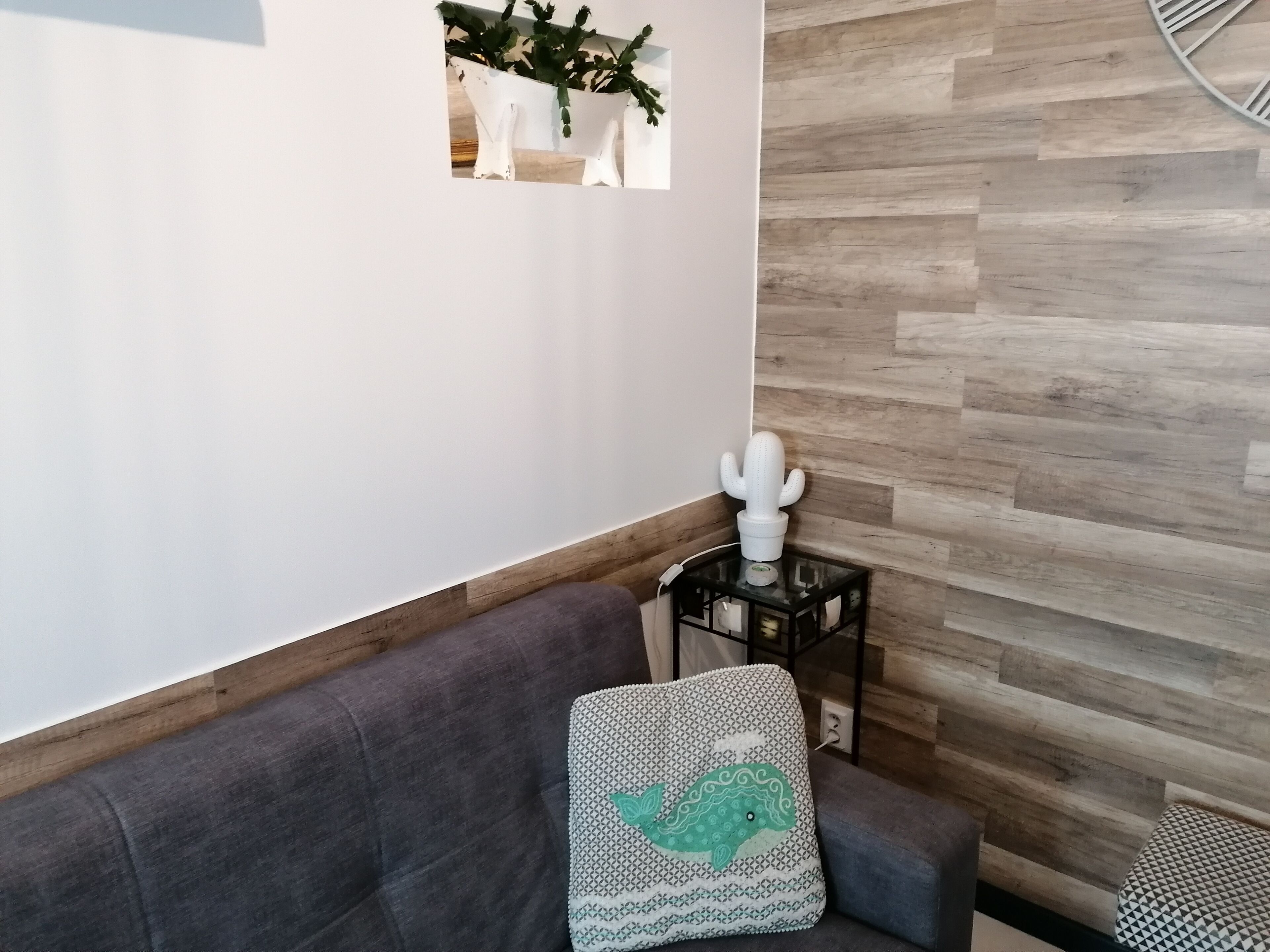 Un salon moderne avec un canapé gris, une décoration en forme de cactus et un coussin à motifs.