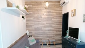 Een moderne woonkamer met een grijze bank, houten wandpanelen, een grote televisie en een bijzettafeltje.