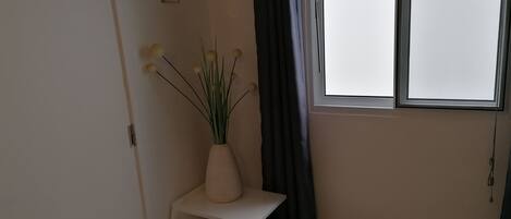 Une pièce avec un bureau blanc, un vase contenant des plantes vertes, un petit cactus et une fenêtre avec des rideaux.