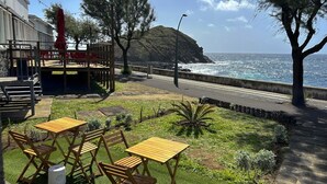 Een terras met buitenmeubilair, uitzicht op de oceaan en een gazon met bomen.