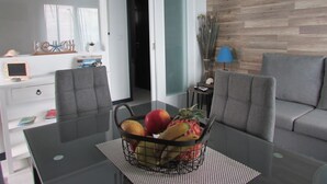 Een moderne woonkamer met een glazen eettafel, grijze banken en een mand met fruit.