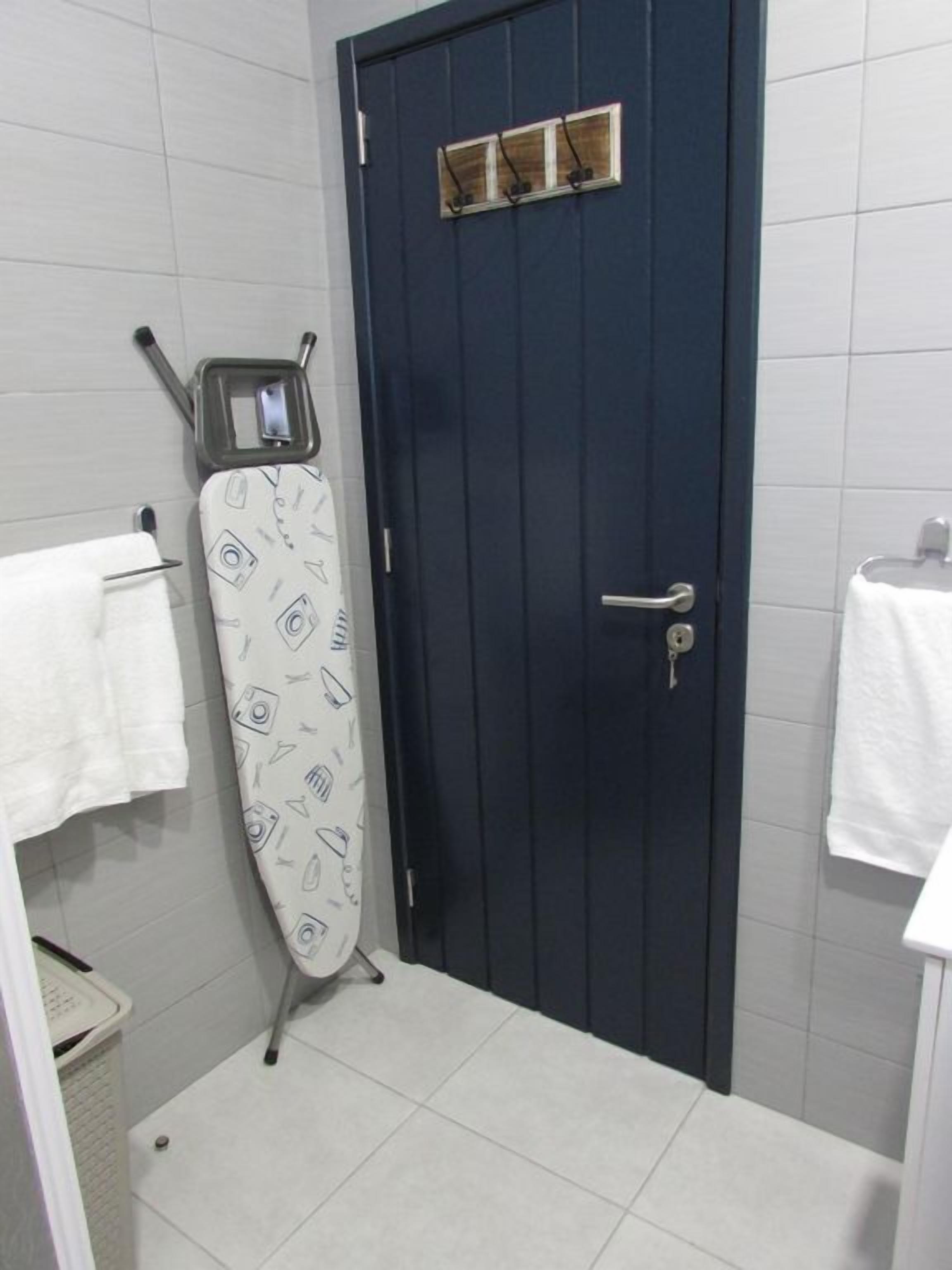 A bathroom with a dark blue door, a white towel hanging on the wall, and an ironing board with a patterned cover.