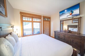 A hotel room with a large bed, wooden headboard, a dresser, a television mounted on the wall, and a balcony with a view of the outdoors. - Lone Eagle 3026 (Keystone)