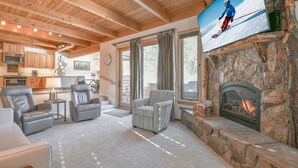 Een gezellige woonkamer met een stenen openhaard, lederen fauteuils, een televisie en een keuken op de achtergrond.