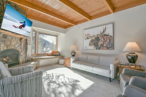 Ein gemütliches Wohnzimmer mit Kamin aus Stein, einem weißen Sofa und einem großen Fernseher, der einen Skifahrer zeigt.