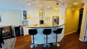 A kitchen with a central island, white cabinetry, and three black bar stools. - Large 4 bedroom, steps from the beach with rooftop patio and jacuzzi. Sleeps 10 (Long Beach)