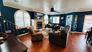 A living room with a fireplace, a ceiling fan, and a staircase. - Large 4 bedroom, steps from the beach with rooftop patio and jacuzzi. Sleeps 10 (Long Beach)