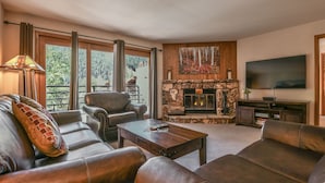 A cozy living room with leather sofas, a fireplace, a TV, and a large window with curtains. - Snow Dance Manor 301 (Keystone)