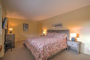 Un dormitorio con cama, mesitas de noche, cómoda y televisor montado en la pared.