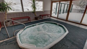A hot tub with a view of a snowy landscape through large windows. - Saints John 2505 (Keystone)