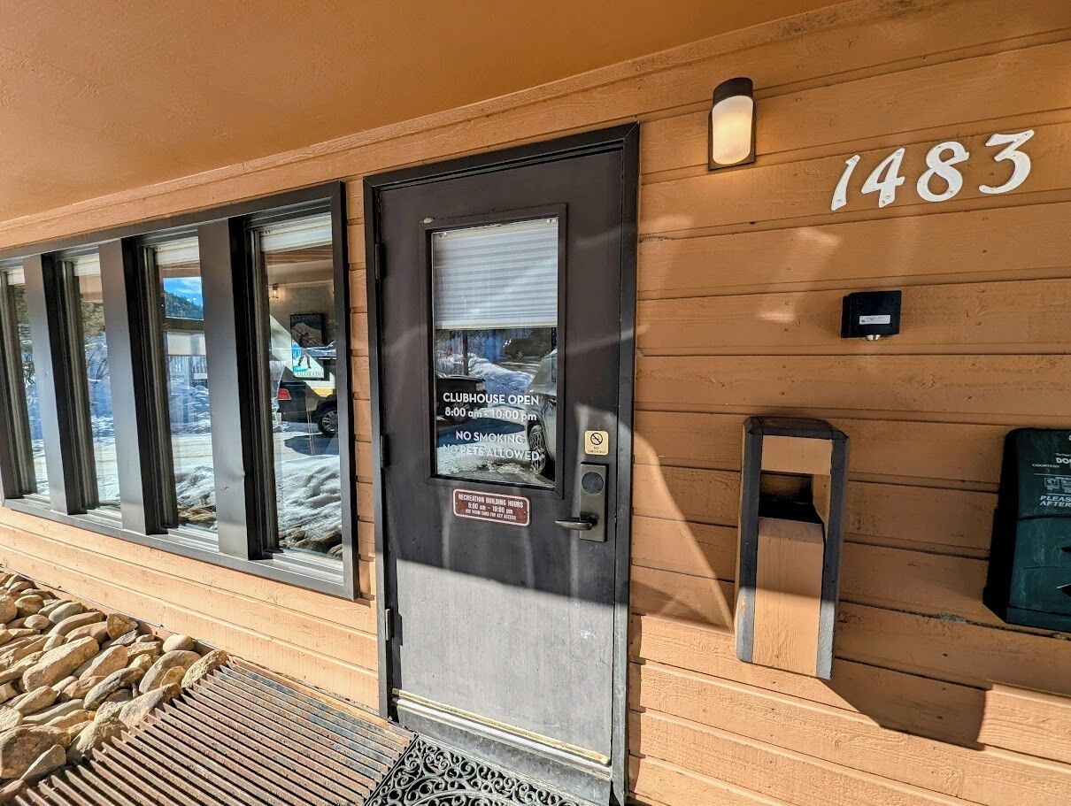 A building entrance with a door labeled "CLUBHOUSE OPEN 8:00 am - 10:00 pm NO SMOKING NO PETS ALLOWED" and the number "1483" on the wall.