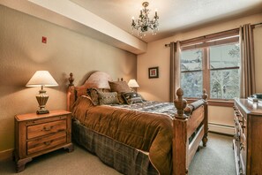 A bedroom with a wooden bed, two bedside tables with lamps, a dresser, and a window with curtains.