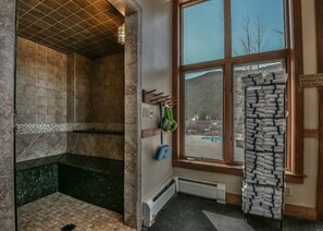 A bathroom with a shower, a towel rack, a window with a view of a pool and trees, and a sign indicating no glass allowed in the pool area.
