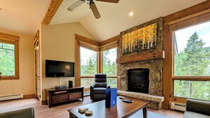 A spacious living room with a stone fireplace, large windows, and a flat-screen TV. - Settlers Creek 6523 (Keystone)