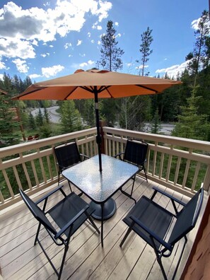 A covered outdoor patio with a table and four chairs, surrounded by a wooden deck and a railing. - Settlers Creek 6523 (Keystone)