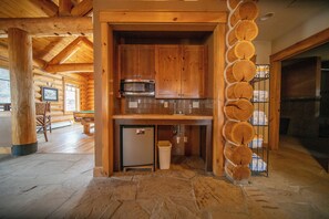 A log cabin interior with a stone floor, wooden cabinets, a microwave, and a fireplace. - Settlers Creek 6523 (Keystone)
