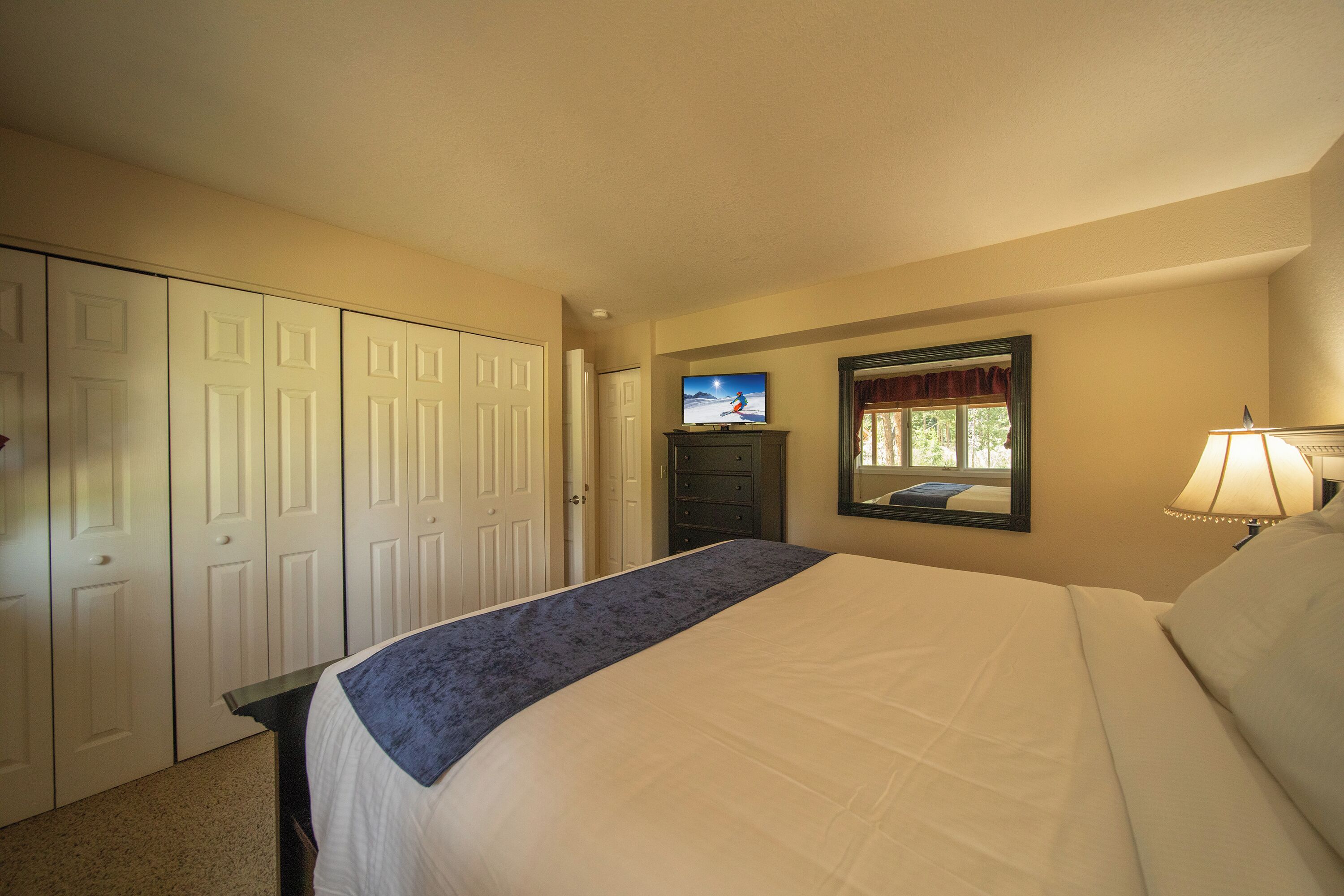 A hotel room with a bed, a television, a dresser, and a mirror.