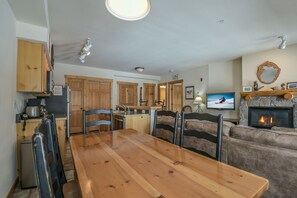 Un salon chaleureux avec une cheminée, un coin repas avec une table et des chaises en bois, et une cuisine dotée de meubles en bois et d’un four à micro-ondes.