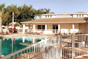 Un espace piscine doté d’une terrasse entourée d’une clôture, de chaises longues et d’un bâtiment avec de nombreuses fenêtres.
