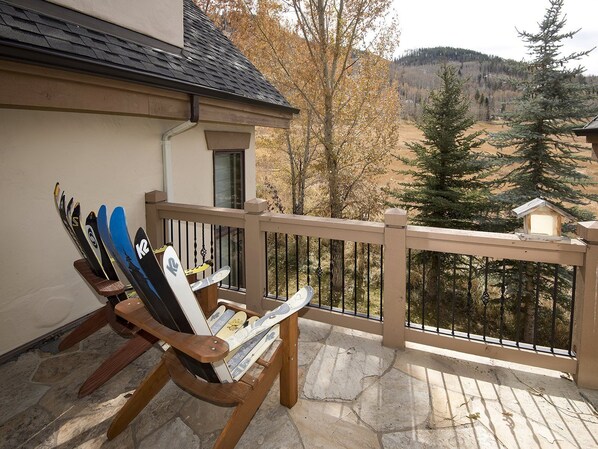 A wooden chair with skis and a snowboard leaning against a balcony railing.