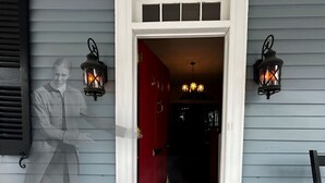 A house entrance with a red door, two wall-mounted lanterns, and a visible interior with a chandelier. - The Federal Quarters (St Marys)