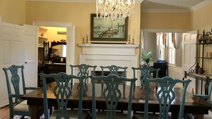 A dining room with a wooden table and chairs, a chandelier, and a fireplace with a painting above it. - The Federal Quarters (St Marys)